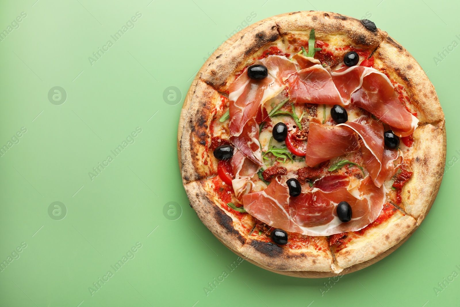 Photo of Tasty pizza with cured ham, olives and sun-dried tomato on green background, top view. Space for text