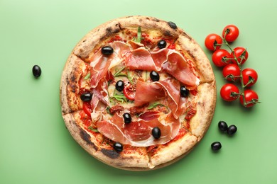 Photo of Tasty pizza with cured ham, olives and tomatoes on green background, top view