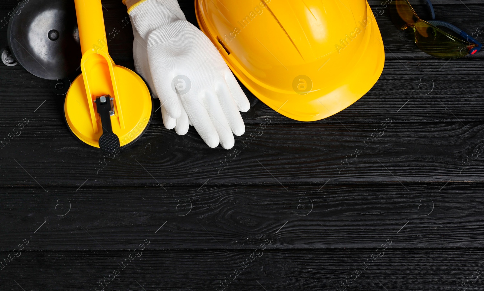 Photo of Hard hat, suction lifters, protective gloves and goggles on black wooden background, flat lay. Space for text