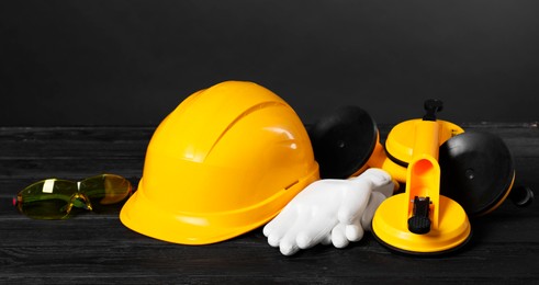 Photo of Hard hat, suction lifters, protective gloves and goggles on black wooden surface against gray background