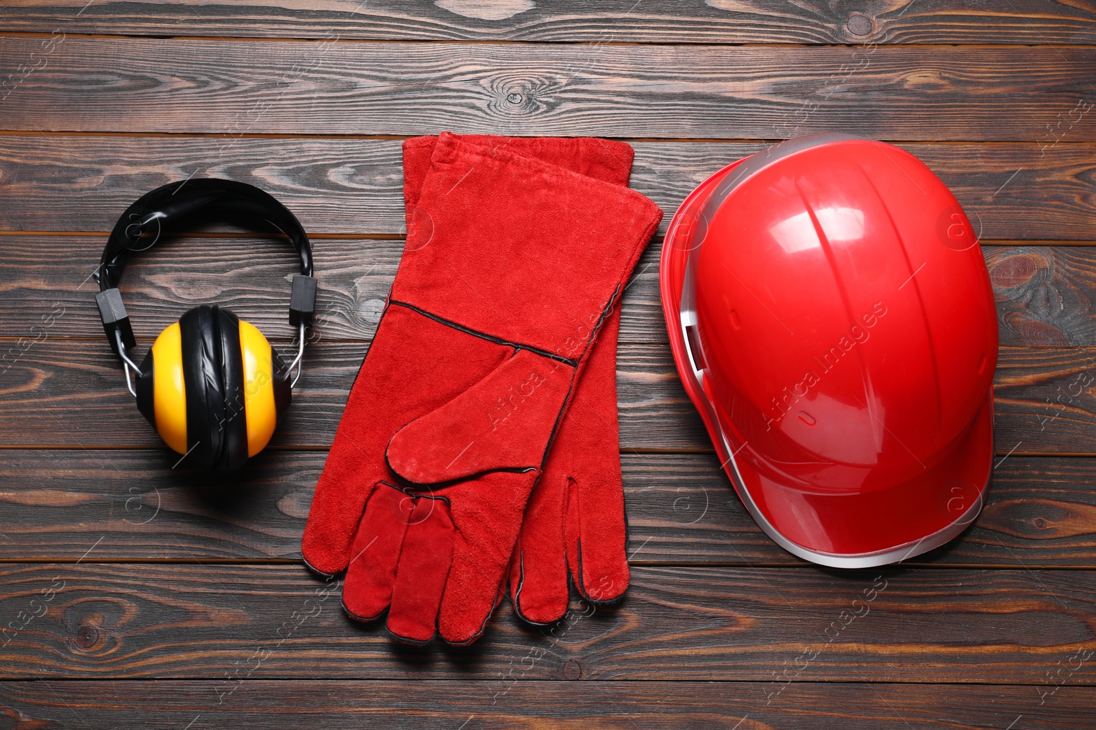 Photo of Hard hat, protective gloves and earmuffs on wooden background, flat lay