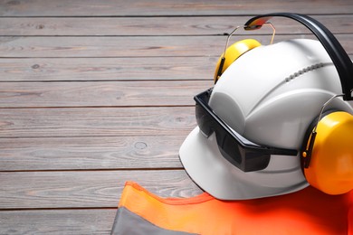 Photo of Reflective vest, hard hat, earmuffs and goggles on wooden background, space for text