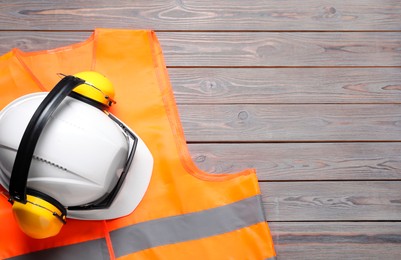 Reflective vest, hard hat, earmuffs and goggles on wooden background, top view. Space for text