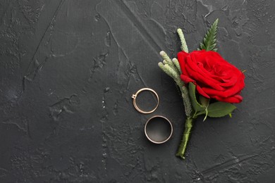 Photo of Stylish red boutonniere and rings on black table, top view. Space for text