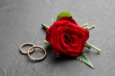 Photo of Stylish red boutonniere and rings on black table