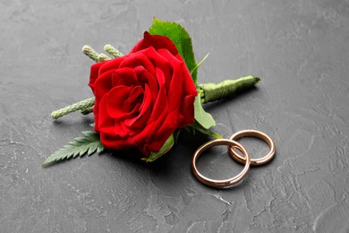 Photo of Stylish red boutonniere and rings on black table