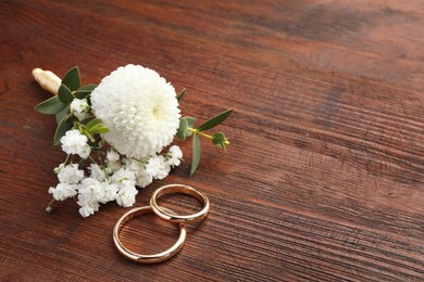 Photo of Small stylish boutonniere and rings on wooden table, space for text