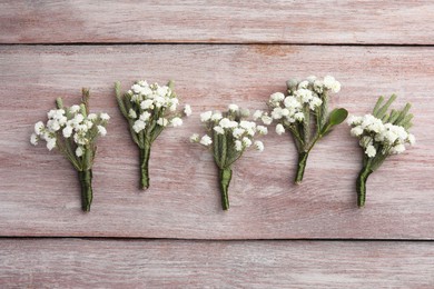 Photo of Many small stylish boutonnieres on light wooden table, flat lay