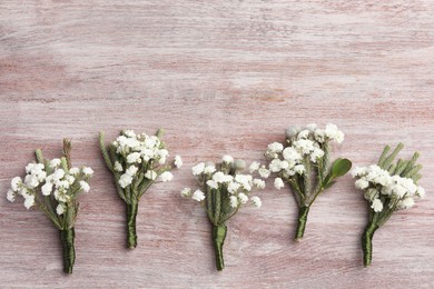 Photo of Many small stylish boutonnieres on light wooden table, flat lay. Space for text