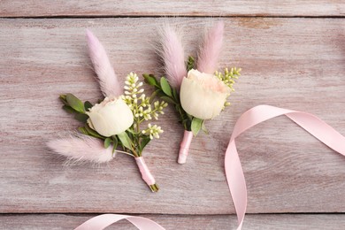 Photo of Small stylish boutonnieres and ribbon on light wooden table, top view