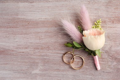Photo of Small stylish boutonniere and rings on light wooden table, top view. Space for text