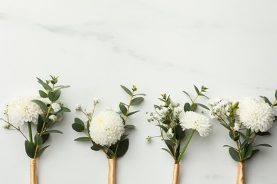 Photo of Small stylish boutonnieres on white marble table, flat lay. Space for text