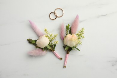 Photo of Small stylish boutonnieres and rings on white marble table, flat lay