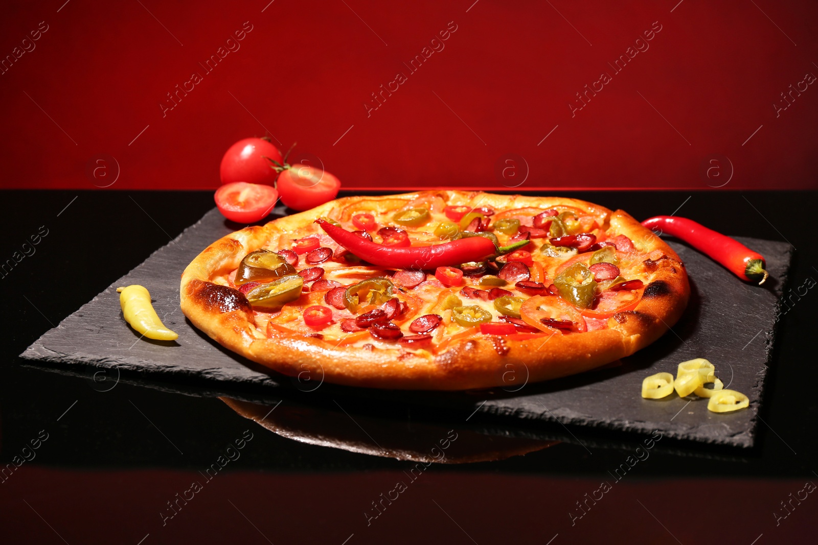 Photo of Delicious pizza Diablo and peppers on slate board against red background