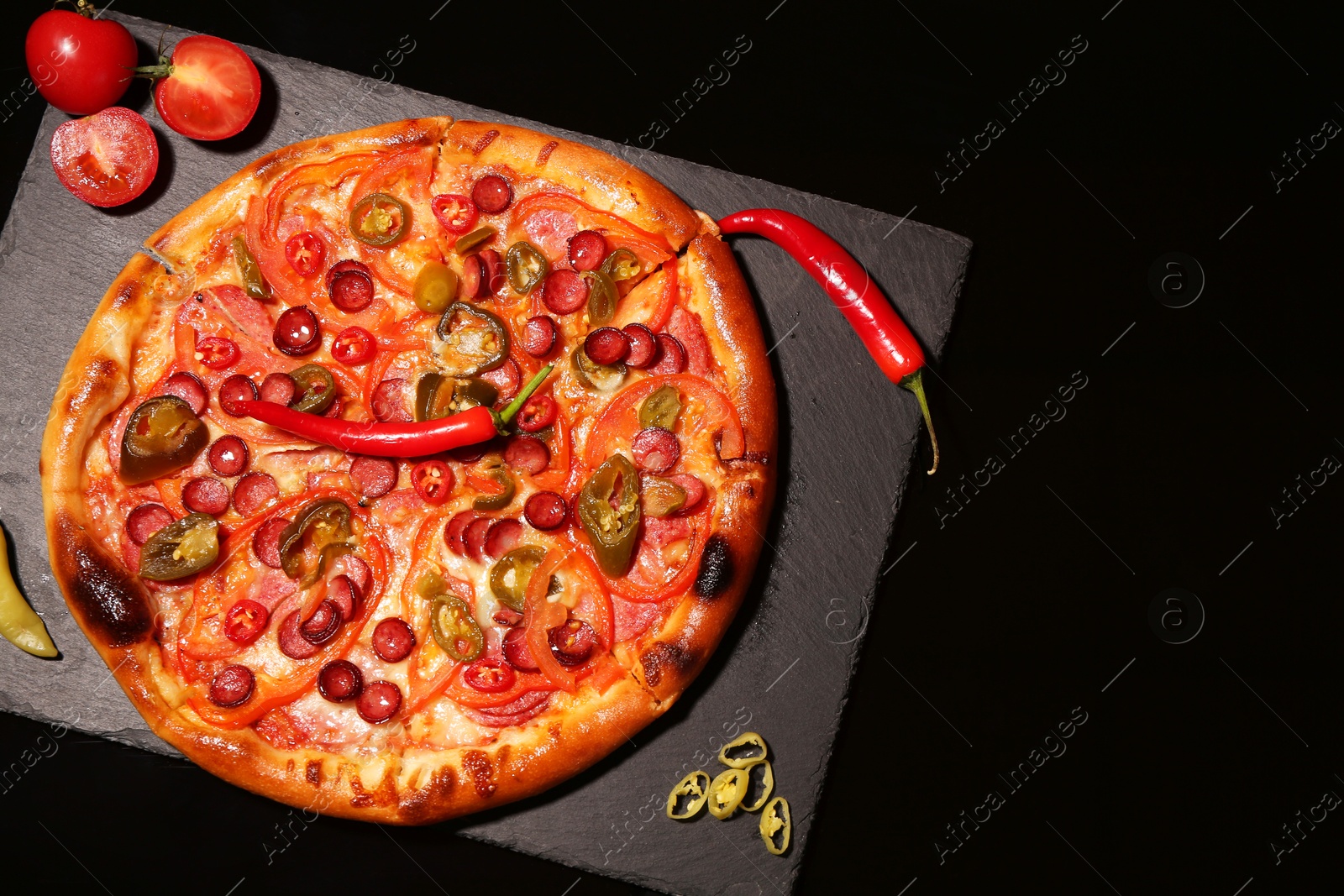 Photo of Slate board with delicious pizza Diablo, tomatoes and peppers on black background, top view. Space for text