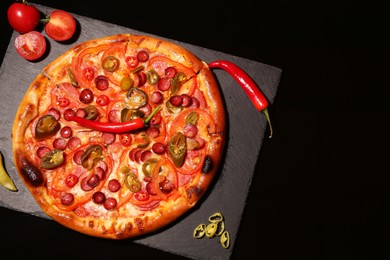 Photo of Slate board with delicious pizza Diablo, tomatoes and peppers on black background, top view. Space for text