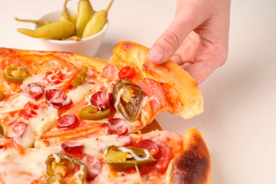 Woman taking piece of delicious pizza Diablo at white textured table, closeup