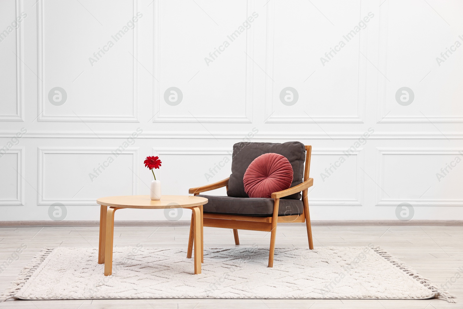 Photo of Comfortable armchair with pillow and coffee table near white wall. Interior design