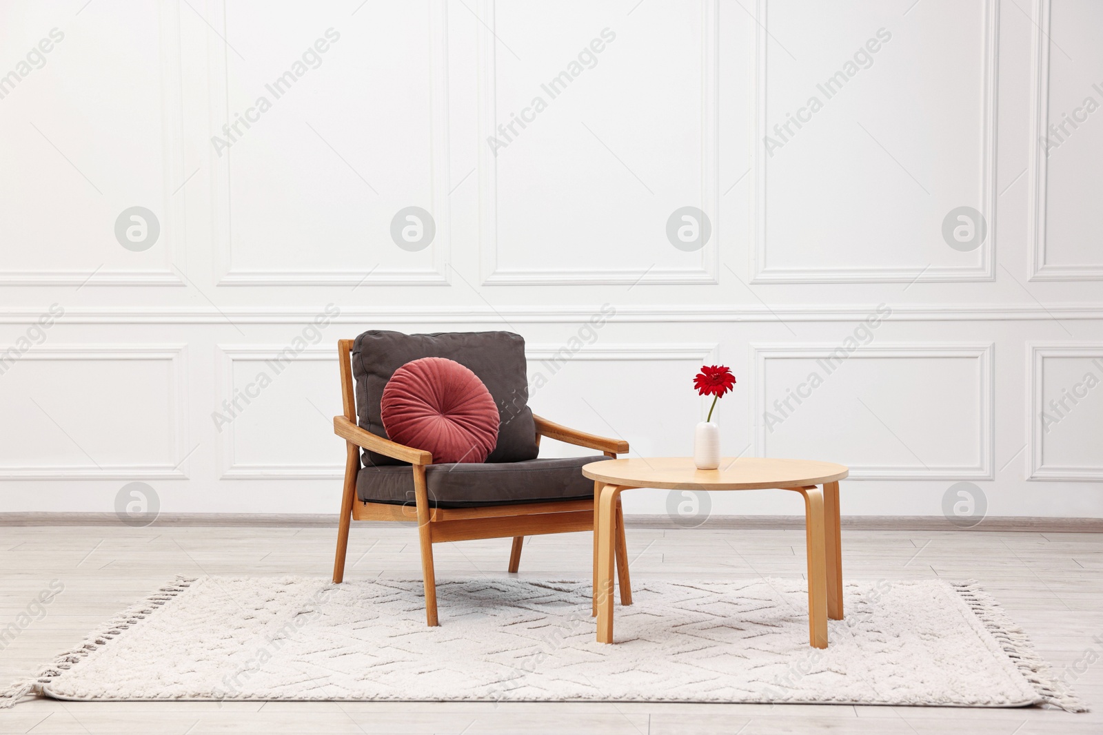 Photo of Comfortable armchair with pillow and coffee table near white wall. Interior design