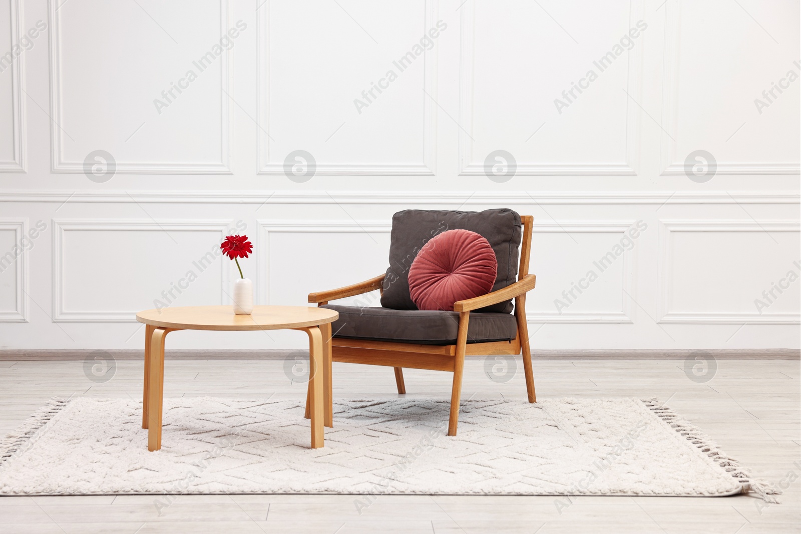 Photo of Comfortable armchair with pillow and coffee table near white wall. Interior design