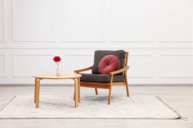 Photo of Comfortable armchair with pillow and coffee table near white wall. Interior design