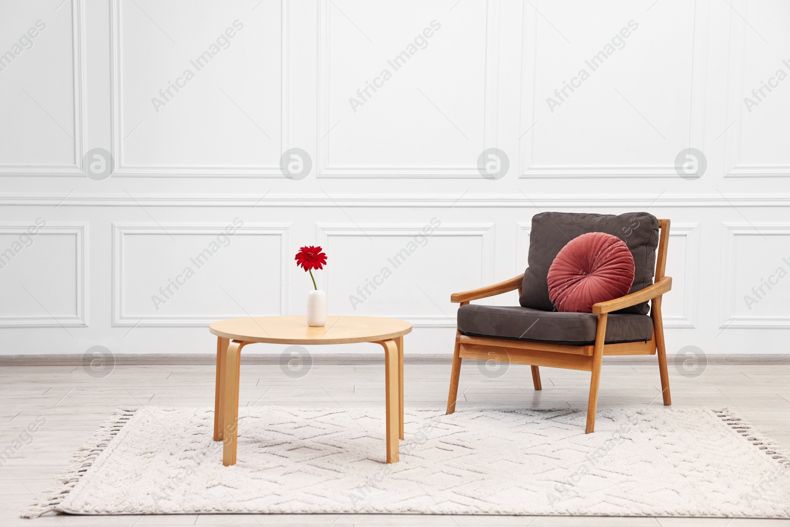 Photo of Comfortable armchair with pillow and coffee table near white wall. Interior design