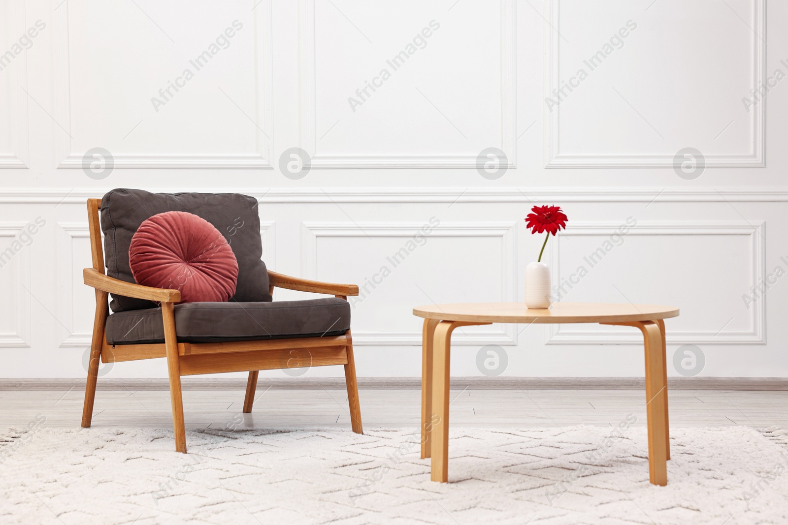 Photo of Comfortable armchair with pillow and coffee table near white wall. Interior design