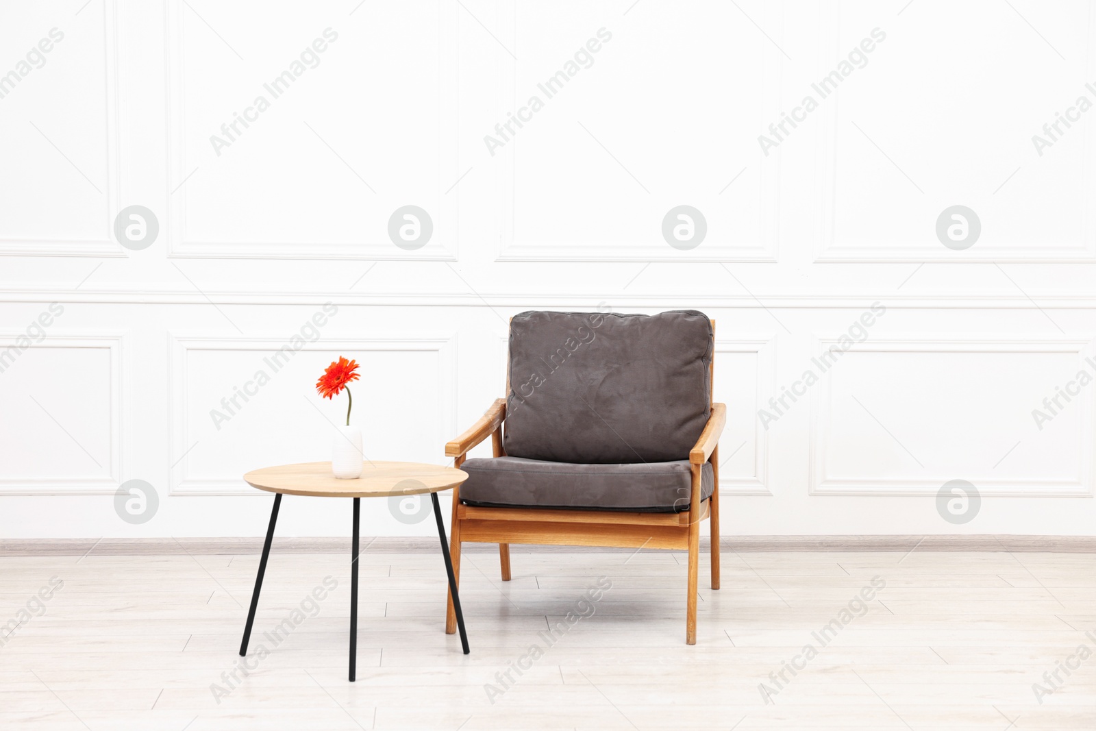 Photo of Comfortable armchair and coffee table with gerbera flower near white wall. Interior design