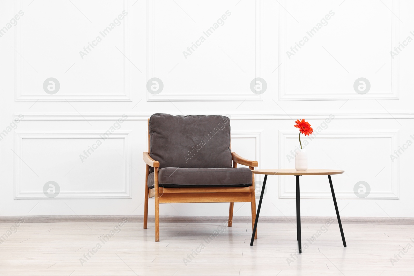 Photo of Comfortable armchair and coffee table with gerbera flower near white wall. Interior design