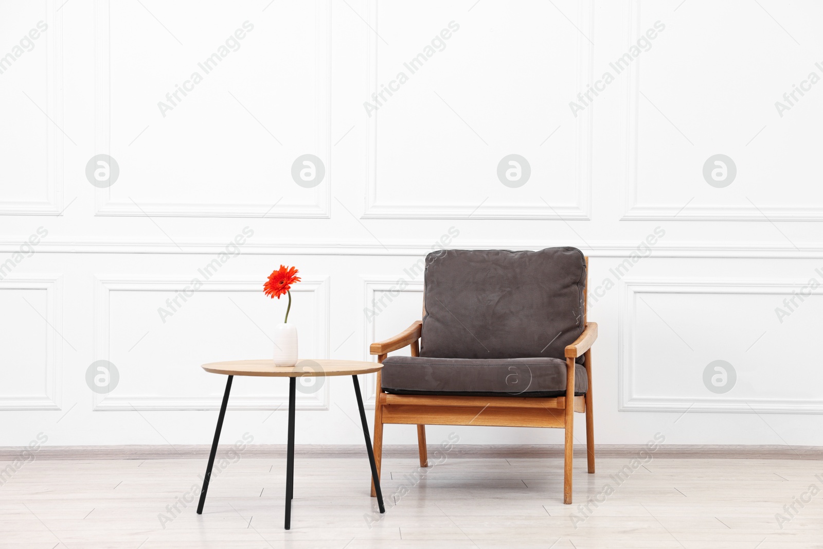 Photo of Comfortable armchair and coffee table with gerbera flower near white wall. Interior design