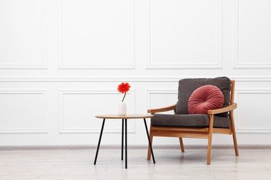 Photo of Comfortable armchair with pillow and coffee table near white wall, space for text. Interior design