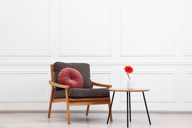 Comfortable armchair with pillow and coffee table near white wall. Interior design