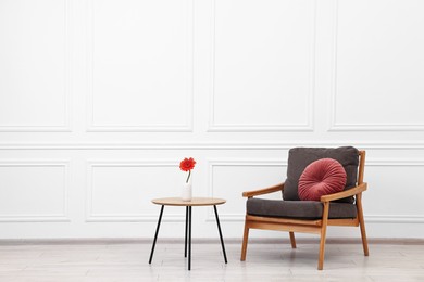 Photo of Comfortable armchair with pillow and coffee table near white wall, space for text. Interior design