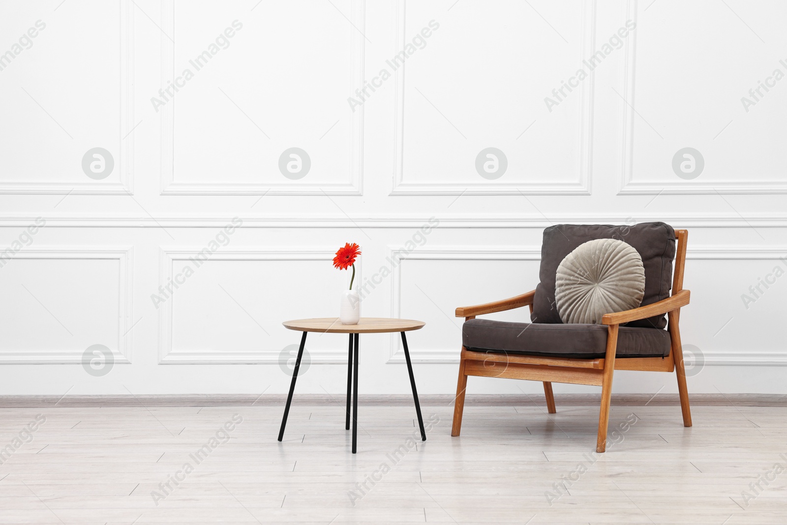 Photo of Comfortable armchair with pillow and coffee table near white wall, space for text. Interior design