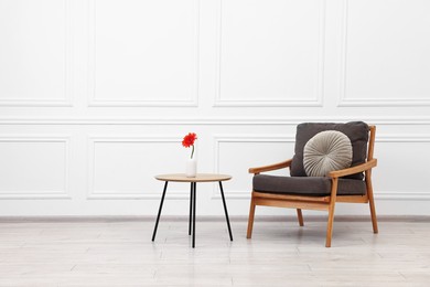 Photo of Comfortable armchair with pillow and coffee table near white wall, space for text. Interior design