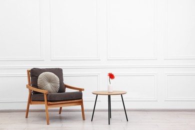 Photo of Comfortable armchair with pillow and coffee table near white wall, space for text. Interior design