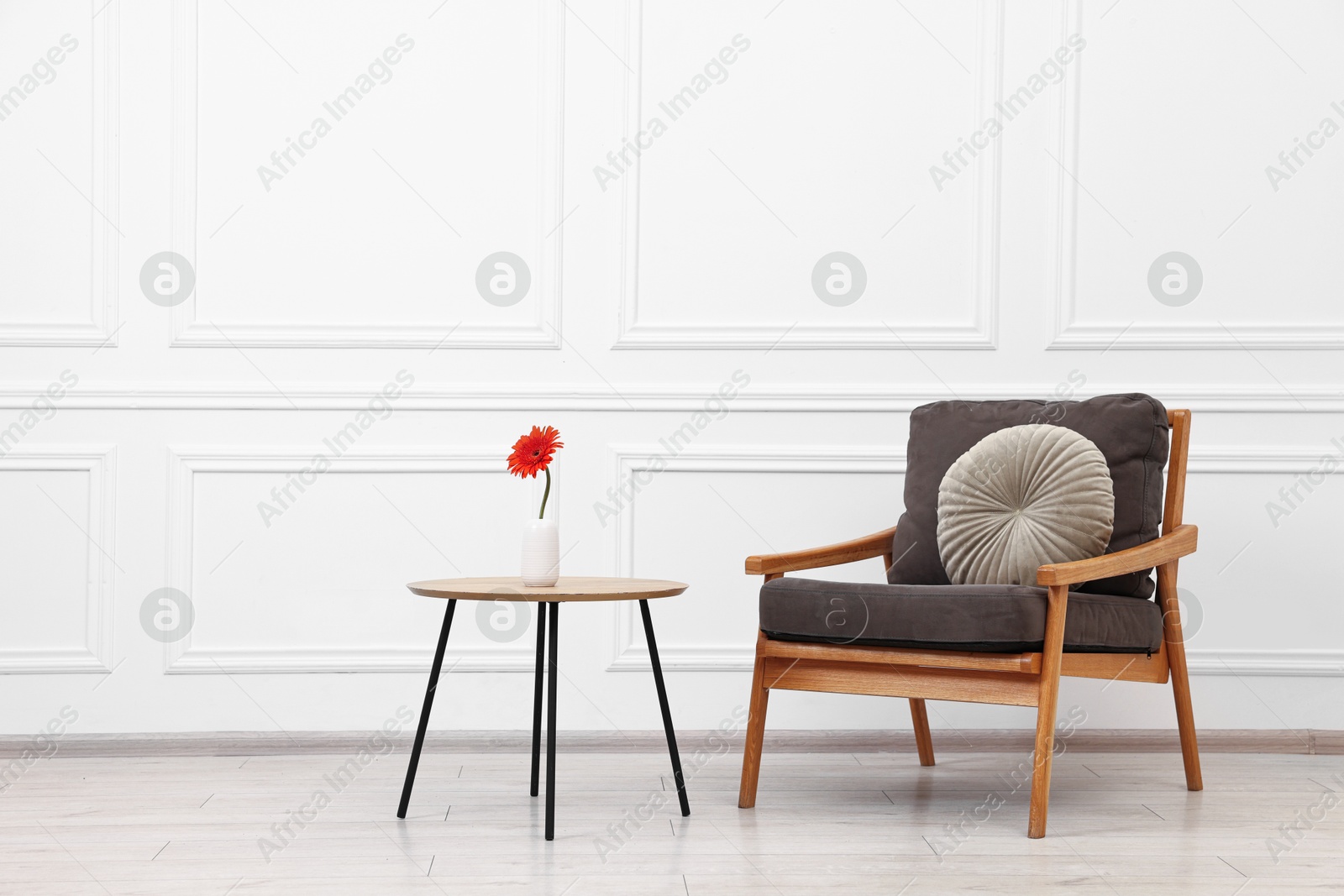 Photo of Comfortable armchair with pillow and coffee table near white wall. Interior design