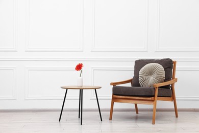 Photo of Comfortable armchair with pillow and coffee table near white wall. Interior design