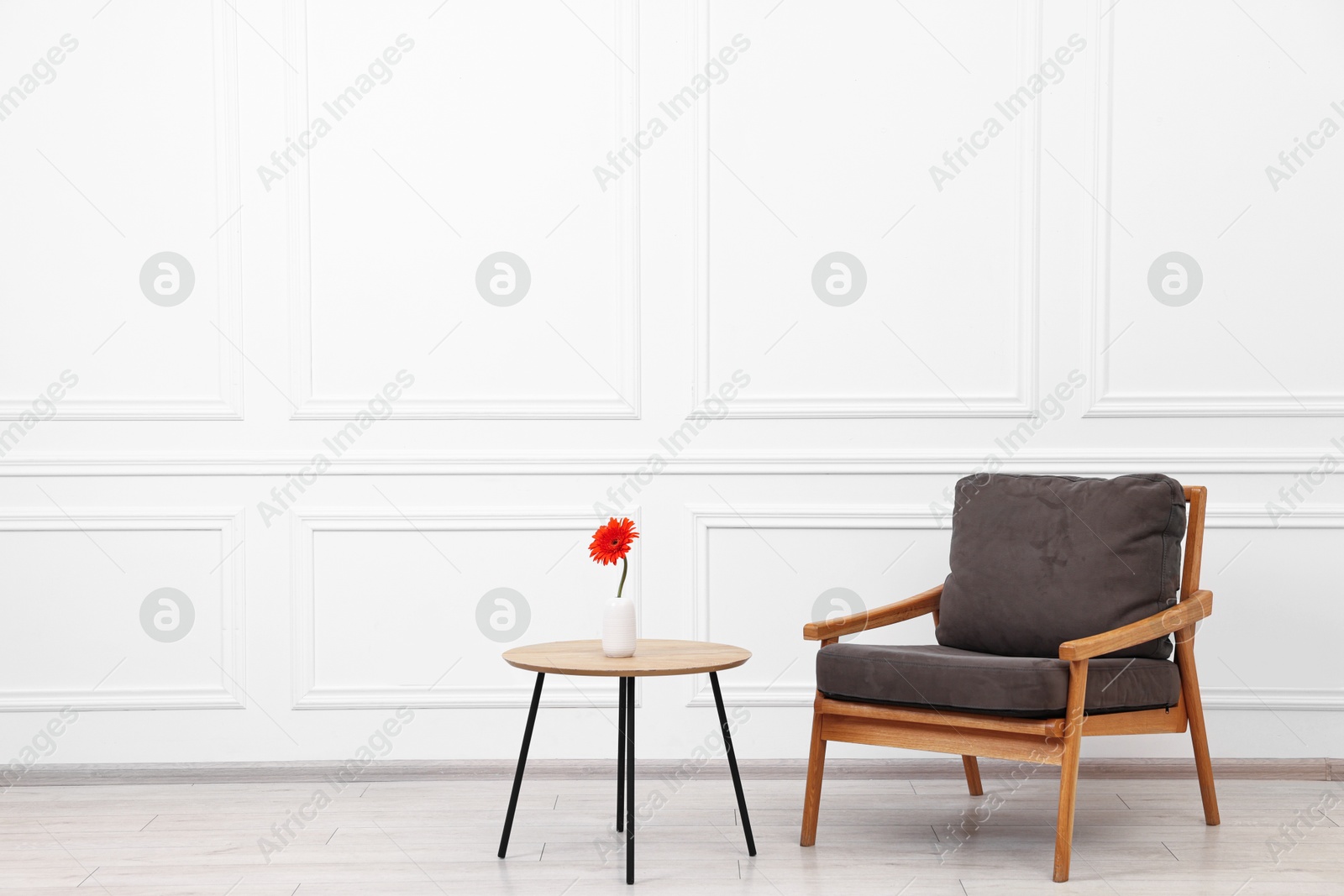 Photo of Comfortable armchair and coffee table with gerbera flower near white wall, space for text. Interior design