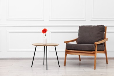 Photo of Comfortable armchair and coffee table with gerbera flower near white wall. Interior design