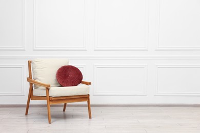 Photo of Comfortable soft armchair with pillow near white wall, space for text