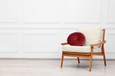 Photo of Comfortable soft armchair with pillow near white wall, space for text