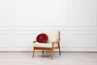 Photo of Comfortable soft armchair with pillow near white wall