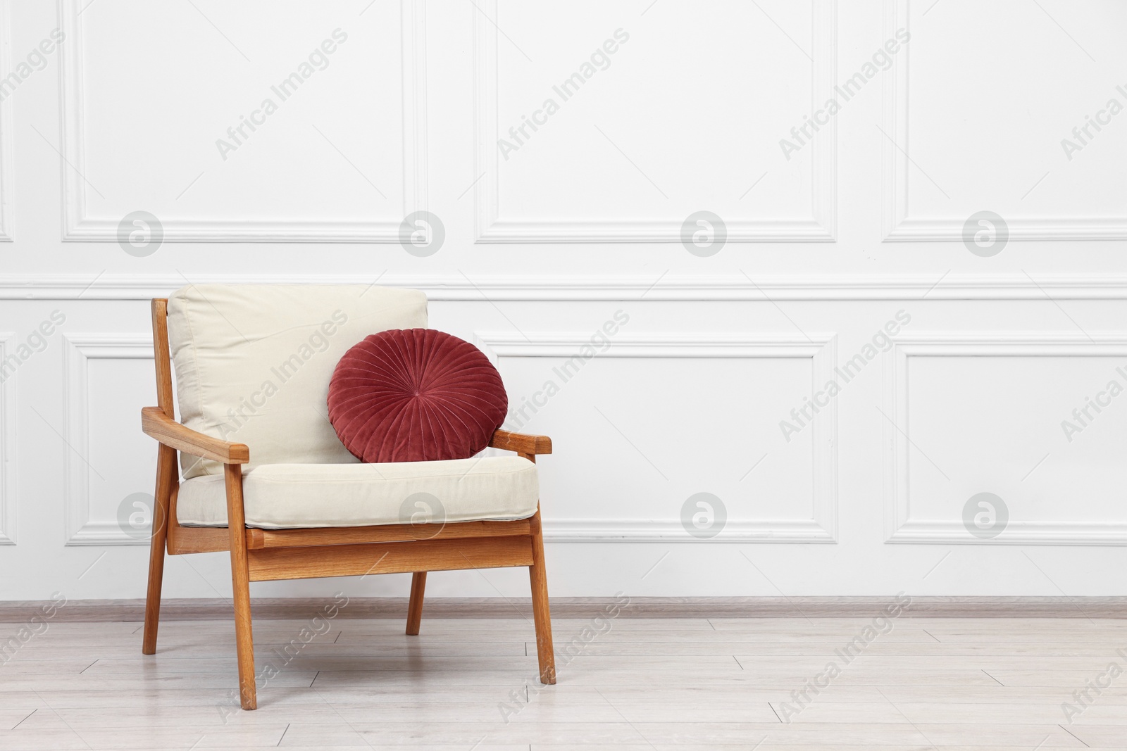 Photo of Comfortable soft armchair with pillow near white wall, space for text