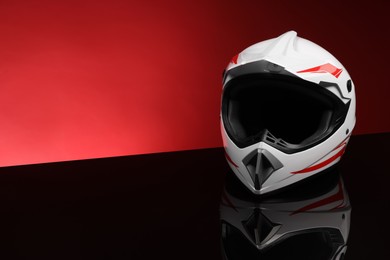 Photo of Modern motorcycle helmet with visor on mirror surface against red background. Space for text