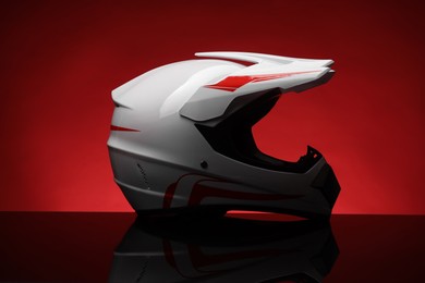 Photo of Modern motorcycle helmet with visor on mirror surface against red background