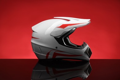 Photo of Modern motorcycle helmet with visor on mirror surface against red background