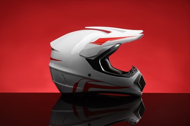 Modern motorcycle helmet with visor on mirror surface against red background