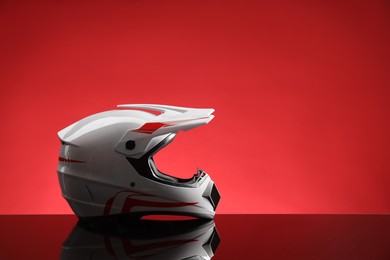 Photo of Modern motorcycle helmet with visor on mirror surface against red background. Space for text