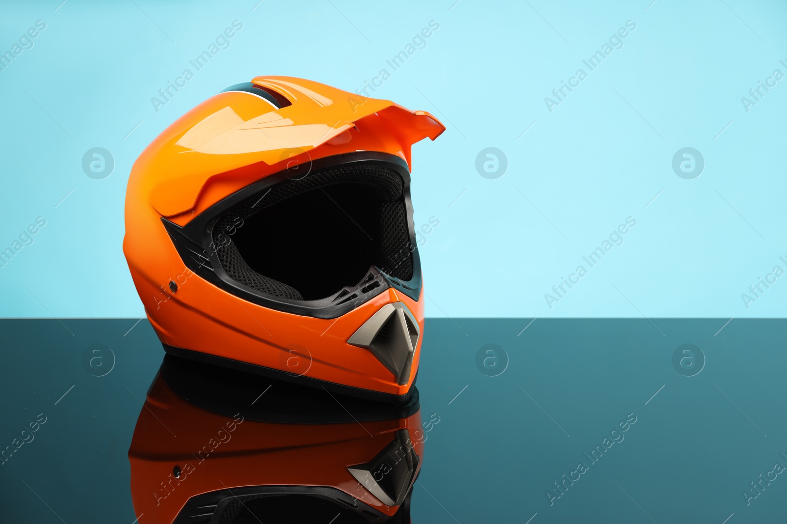 Photo of Modern motorcycle helmet with visor on mirror surface against light blue background. Space for text